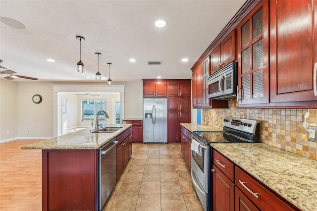 kitchen featuring appliances with stainless steel finishes, pendant lighting, sink, decorative backsplash, and a kitchen island with sink