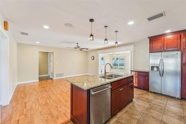 kitchen with appliances with stainless steel finishes, decorative light fixtures, sink, a kitchen island with sink, and light stone counters