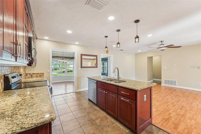 kitchen with sink, light stone counters, appliances with stainless steel finishes, an island with sink, and pendant lighting