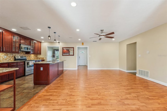 kitchen featuring stainless steel appliances, an island with sink, pendant lighting, and light hardwood / wood-style floors