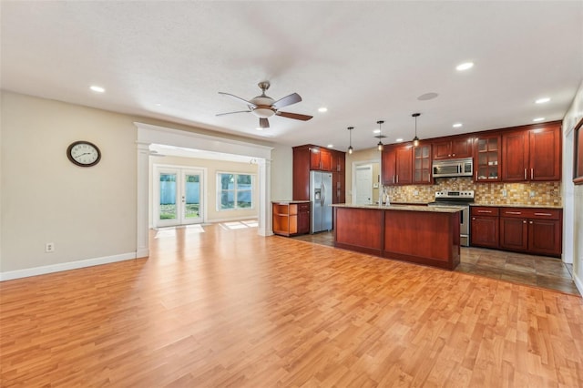 kitchen featuring pendant lighting, stainless steel appliances, light hardwood / wood-style floors, and a center island with sink