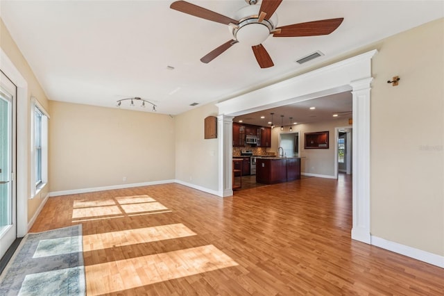 unfurnished living room featuring ceiling fan, plenty of natural light, wood-type flooring, and ornate columns