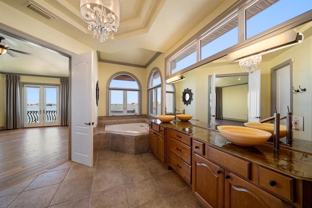 bathroom with vanity, a relaxing tiled tub, a raised ceiling, crown molding, and french doors