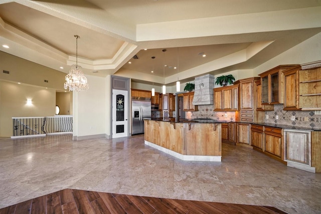 kitchen with hanging light fixtures, stainless steel built in refrigerator, a raised ceiling, and decorative backsplash