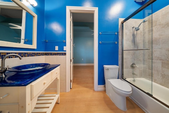 full bathroom with toilet, bath / shower combo with glass door, tile walls, vanity, and hardwood / wood-style flooring