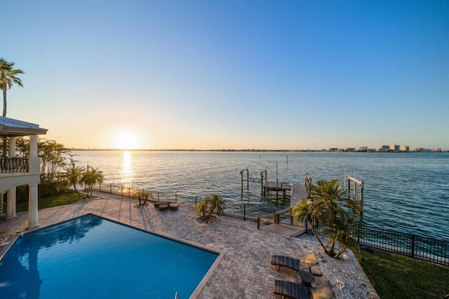 pool at dusk featuring a water view, a patio, and a boat dock