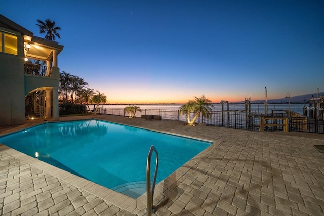 pool at dusk featuring a water view and a patio area