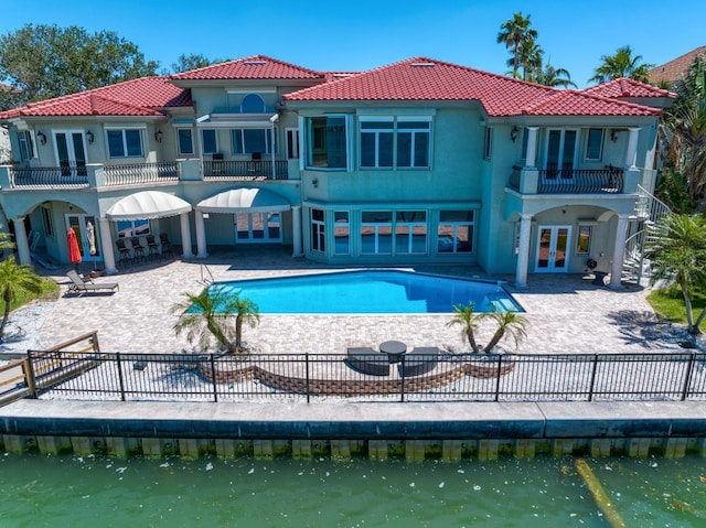 back of house featuring a fenced backyard, a patio area, a tile roof, a balcony, and french doors