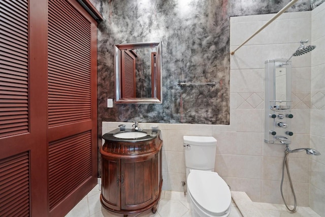 bathroom with tiled shower, vanity, tile walls, and toilet