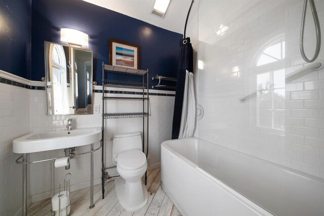 full bathroom with tile walls, a sink, toilet, and shower / washtub combination