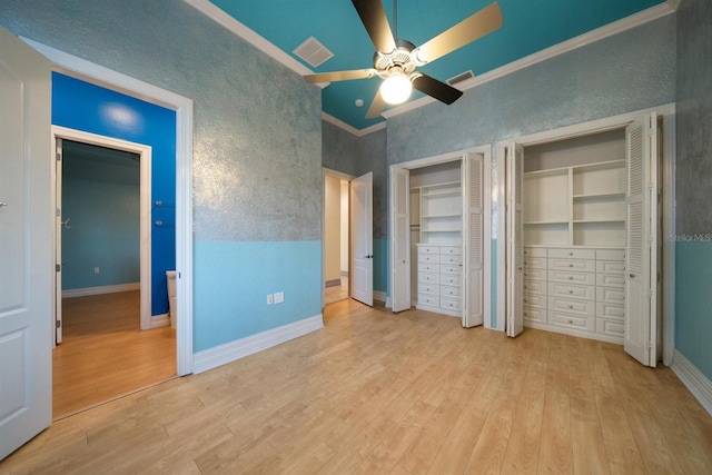 unfurnished bedroom featuring ornamental molding, wood finished floors, two closets, and visible vents
