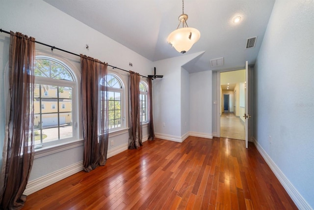 empty room with wood finished floors, visible vents, and baseboards