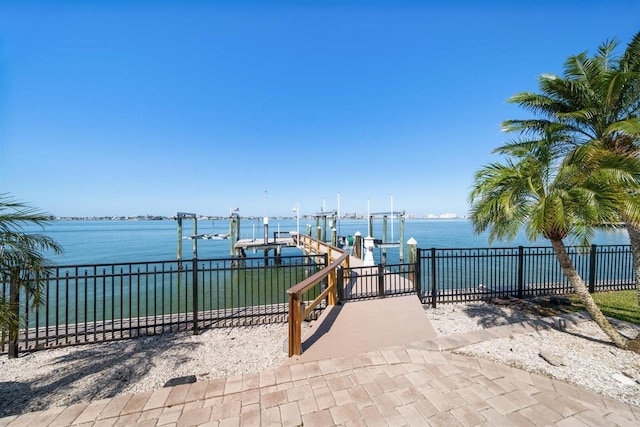 view of patio with a water view, fence, boat lift, and a dock