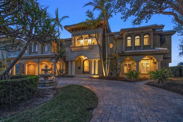 view of front of home with a balcony, curved driveway, and stucco siding