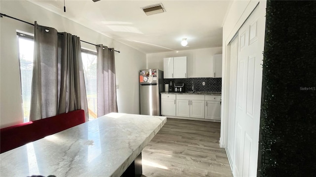 kitchen with white cabinets, backsplash, stainless steel fridge, light stone counters, and light hardwood / wood-style floors