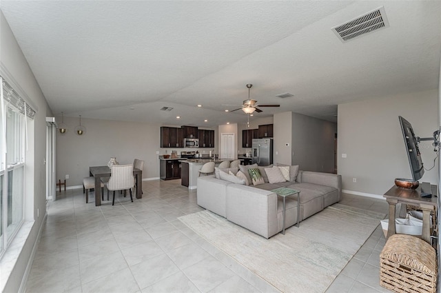 tiled living room featuring ceiling fan, lofted ceiling, and a textured ceiling