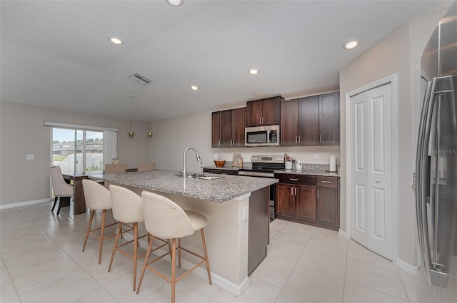 kitchen with dark brown cabinetry, sink, a breakfast bar area, appliances with stainless steel finishes, and a kitchen island with sink