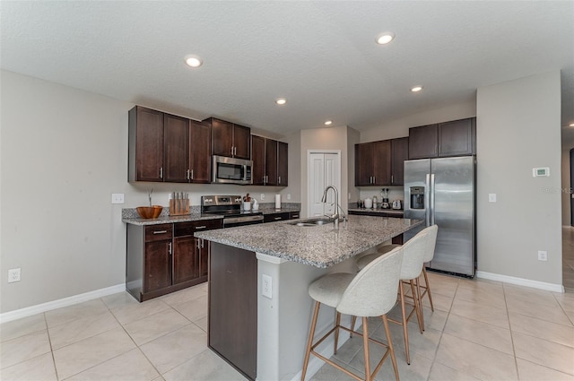 kitchen featuring sink, appliances with stainless steel finishes, a kitchen island with sink, dark brown cabinetry, and a kitchen bar