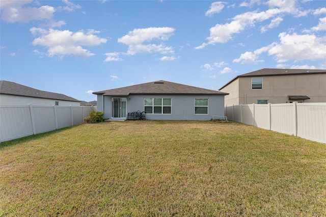 back of house with a fenced backyard, a lawn, and stucco siding