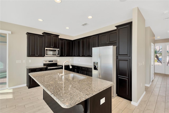 kitchen featuring stainless steel appliances, sink, light stone countertops, and a kitchen island with sink