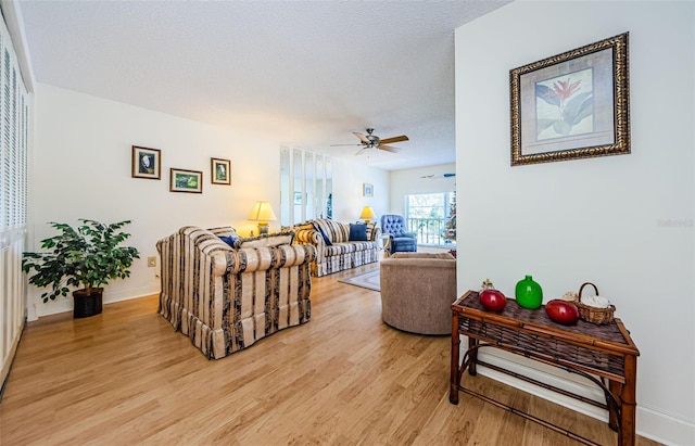 living room featuring ceiling fan, a textured ceiling, and light wood-type flooring