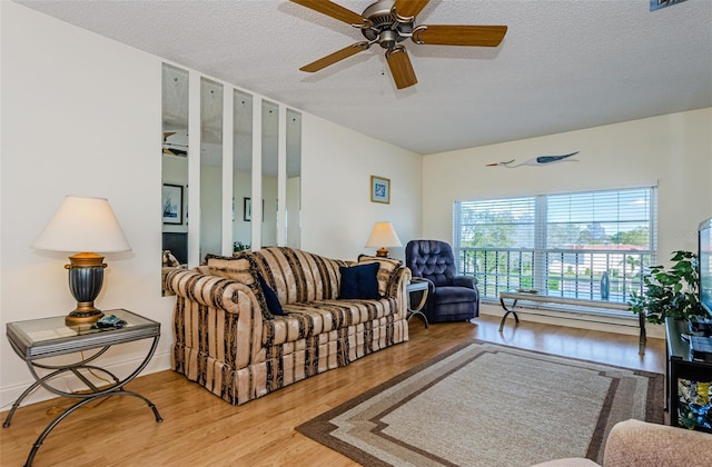 living room with ceiling fan, a textured ceiling, and light hardwood / wood-style floors