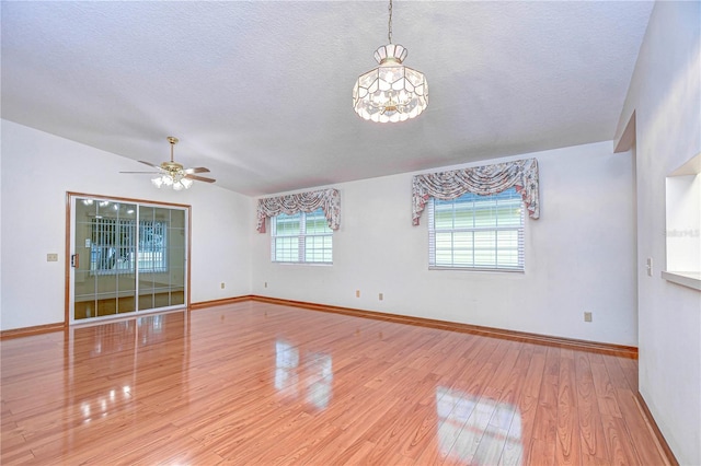 spare room with vaulted ceiling, ceiling fan with notable chandelier, a textured ceiling, and light hardwood / wood-style flooring