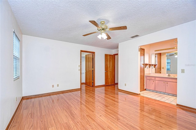 interior space with ceiling fan, a textured ceiling, light hardwood / wood-style floors, and ensuite bath