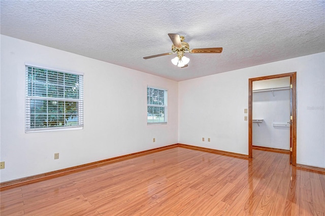 unfurnished bedroom featuring multiple windows, a walk in closet, light hardwood / wood-style flooring, and a textured ceiling