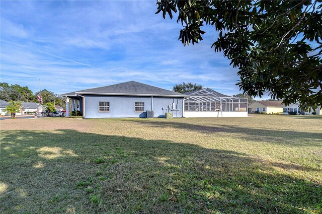 rear view of property featuring central AC unit, glass enclosure, and a lawn