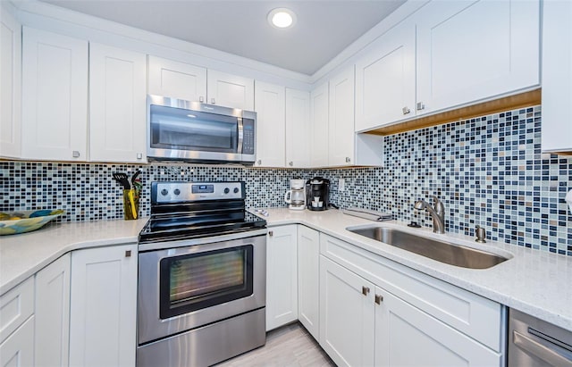 kitchen featuring appliances with stainless steel finishes, tasteful backsplash, white cabinetry, sink, and light hardwood / wood-style flooring