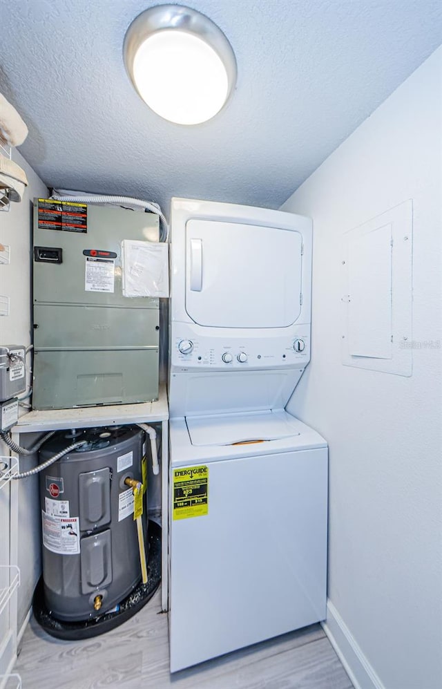 laundry room featuring stacked washer and dryer, light hardwood / wood-style flooring, electric water heater, and a textured ceiling