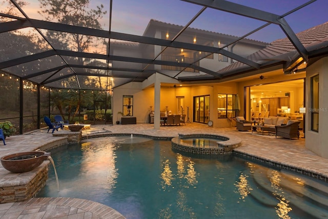 pool at dusk with an in ground hot tub, glass enclosure, a patio, and an outdoor living space with a fire pit