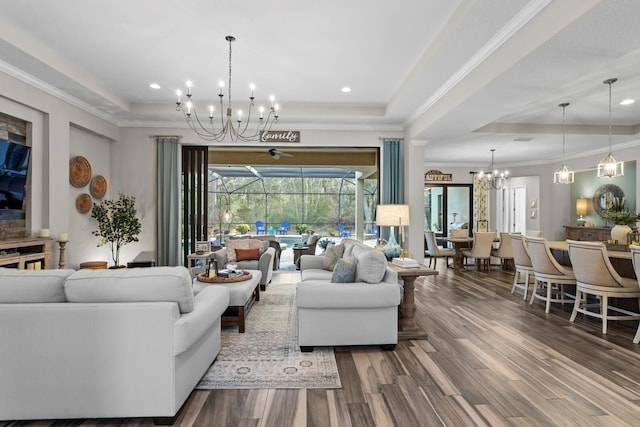 living room featuring a raised ceiling, wood-type flooring, ornamental molding, and an inviting chandelier