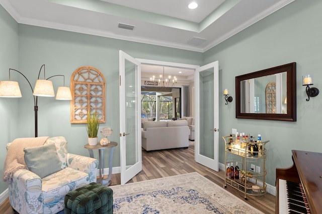 living area with a chandelier, hardwood / wood-style flooring, ornamental molding, a raised ceiling, and french doors