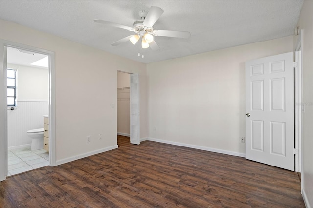 unfurnished bedroom featuring dark wood-type flooring, connected bathroom, a textured ceiling, a closet, and ceiling fan