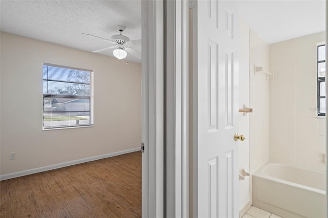 bathroom featuring hardwood / wood-style flooring, ceiling fan, tiled shower / bath combo, and a textured ceiling