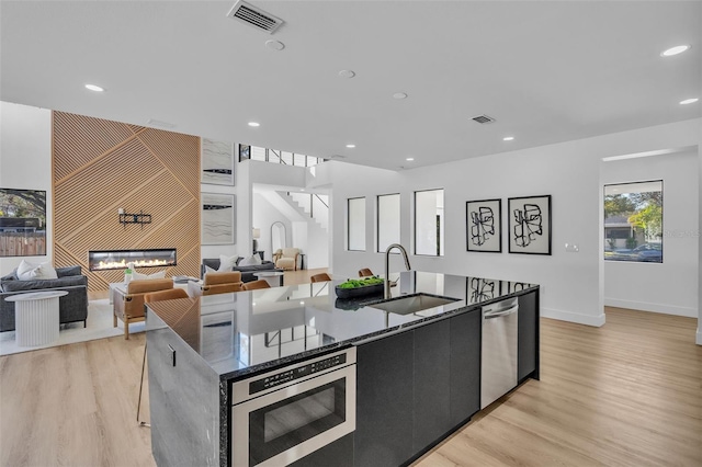 kitchen with a tiled fireplace, sink, an island with sink, and appliances with stainless steel finishes