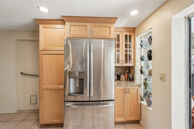 kitchen featuring light stone counters, stainless steel fridge, light brown cabinetry, and light tile patterned floors