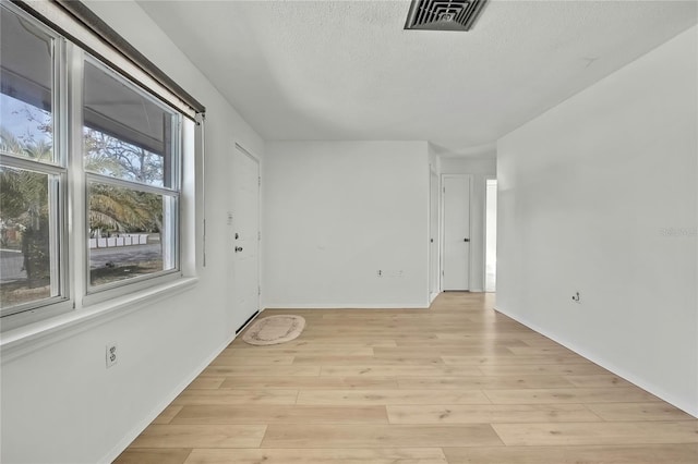 empty room with a textured ceiling and light hardwood / wood-style flooring