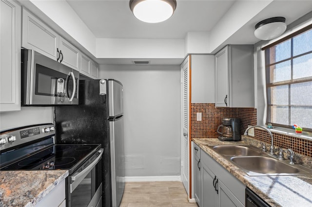 kitchen featuring sink, gray cabinets, stainless steel appliances, light stone countertops, and backsplash