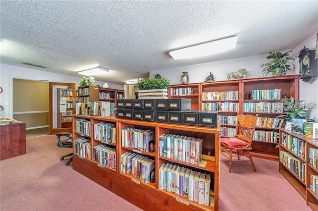 sitting room with wall of books, a textured ceiling, visible vents, and carpet flooring