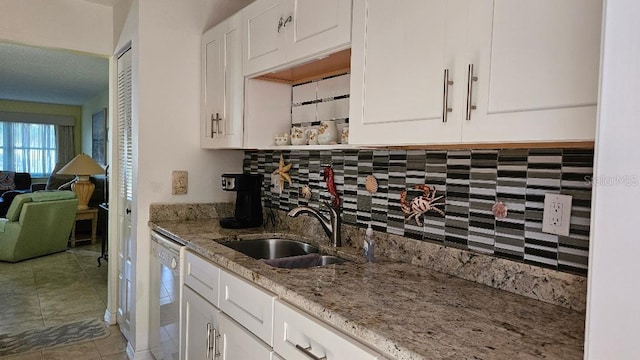 kitchen featuring dishwashing machine, decorative backsplash, a sink, light stone counters, and white cabinets