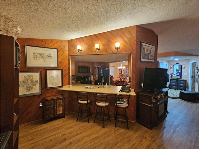 bar featuring a chandelier, a textured ceiling, wooden walls, hardwood / wood-style floors, and black appliances