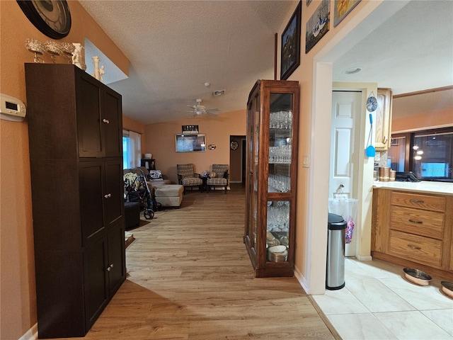 corridor featuring light hardwood / wood-style floors, vaulted ceiling, and a textured ceiling