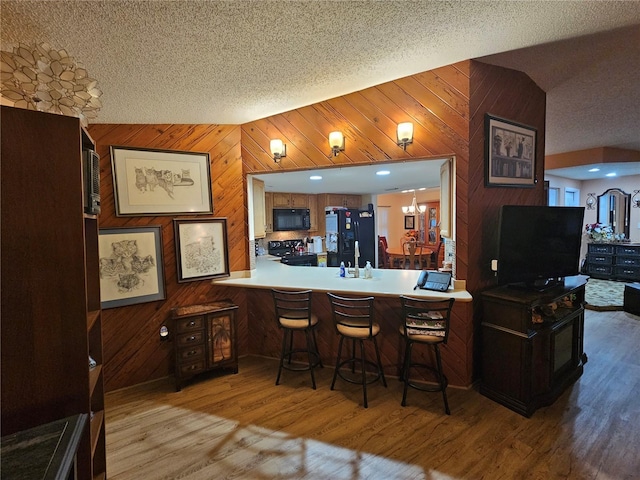 kitchen with light hardwood / wood-style floors, black appliances, a textured ceiling, a kitchen bar, and kitchen peninsula