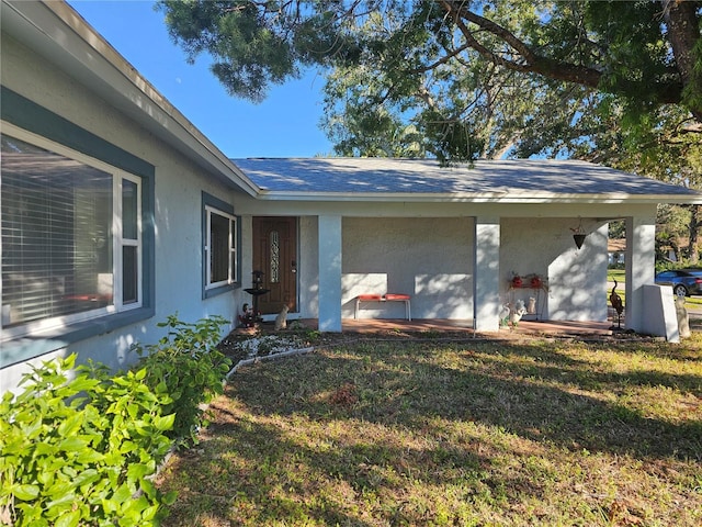 entrance to property with roof with shingles, a lawn, and stucco siding