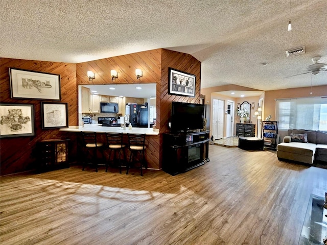7711 Innis Ct, Saint Petersburg, FL 33709 - living room featuring vaulted ceiling, a ceiling fan, wooden walls, wood finished floors, and visible vents