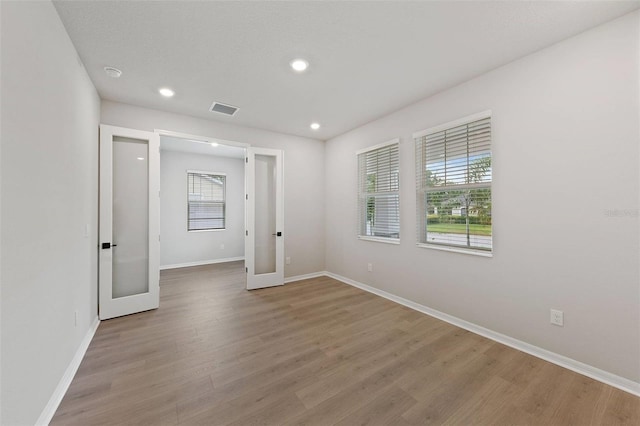 empty room with a healthy amount of sunlight, light hardwood / wood-style floors, and french doors