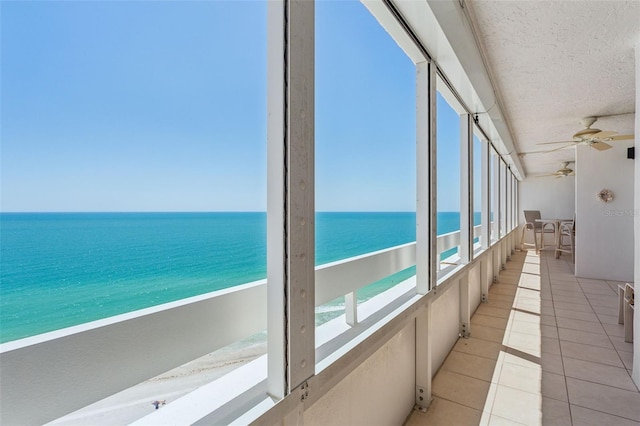 sunroom / solarium featuring ceiling fan, a beach view, a healthy amount of sunlight, and a water view